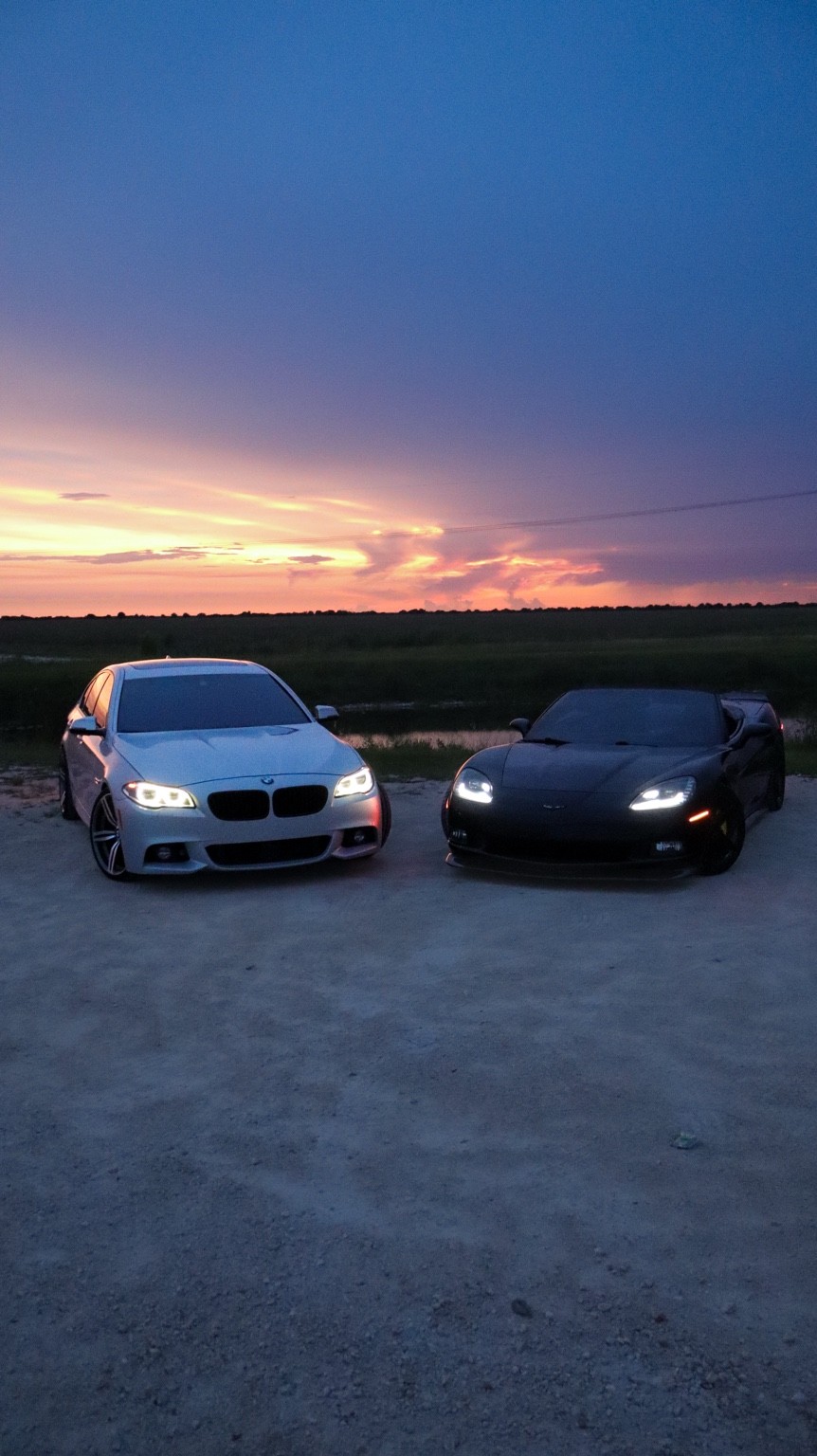 BMW and Corvette parked beneath a colorful sunset